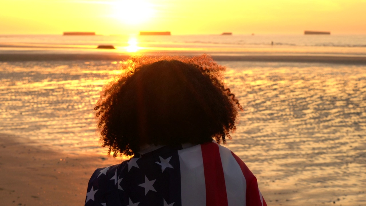 混合种族，混血，非裔美国女孩，青少年，女性，年轻的女人在日落或日出的海滩上拿着美国星条旗视频素材