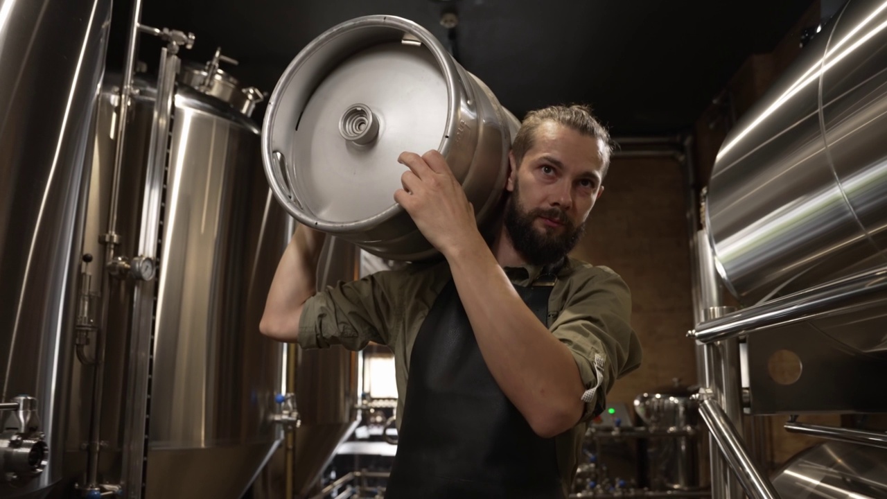 一名正在工作的男性酿酒师背着装满啤酒的小桶走过啤酒罐视频下载