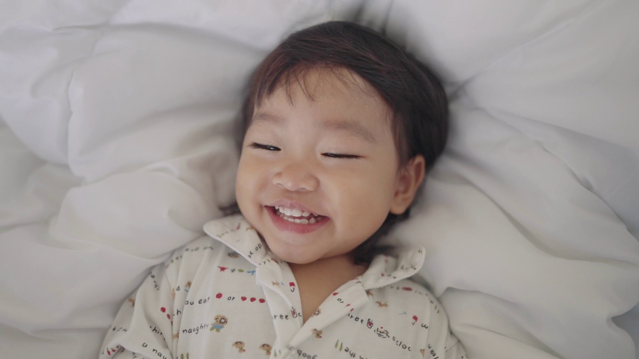 亚洲宝宝笑着，享受着和妈妈在舒适的床上玩耍，简单的生活和家庭生活视频素材