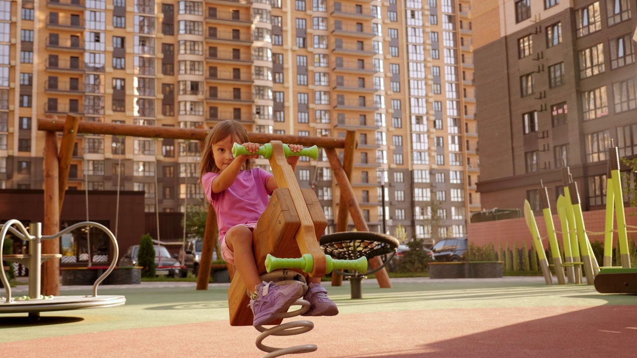 一个小女孩正在操场的弹簧上的木制摇椅上荡秋千。视频下载