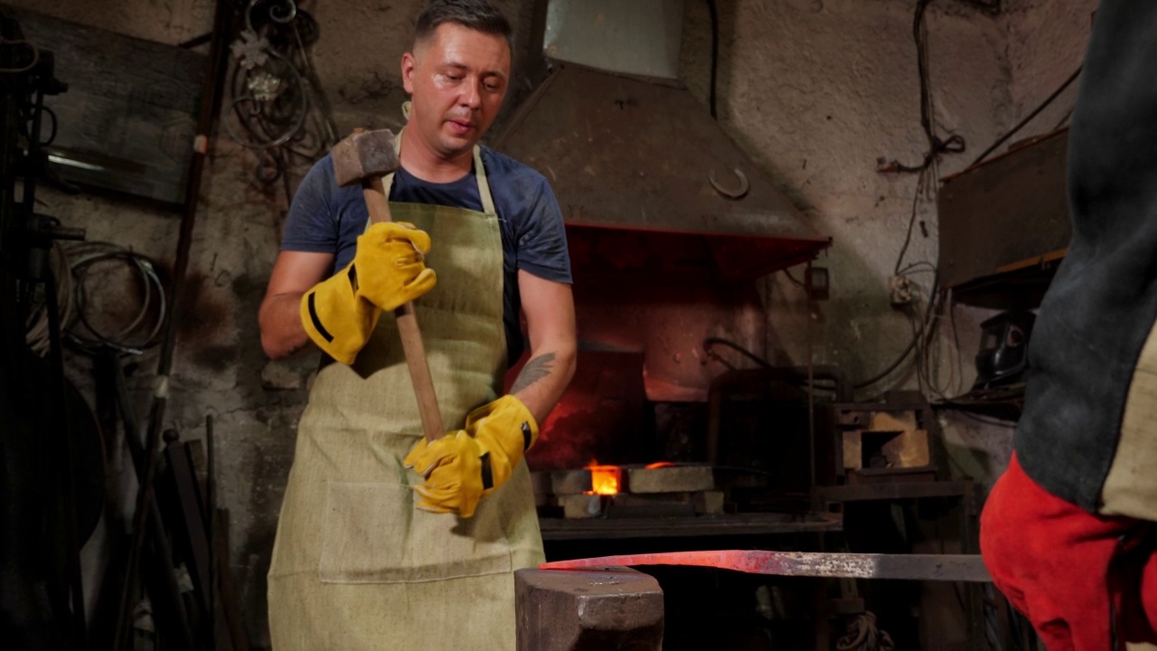 在一个古老的铁匠铺里，两个铁匠在铁砧上敲打着滚烫的金属。视频下载