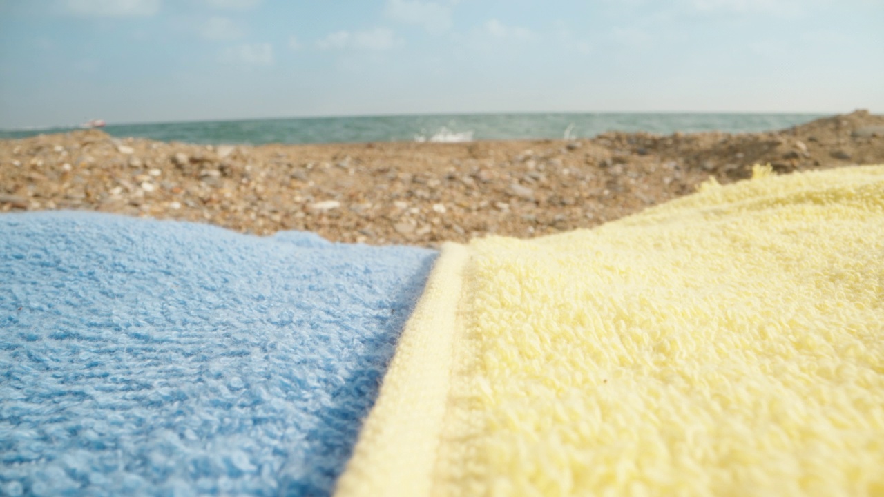 蓝色和黄色的毛巾在海边，质感。镜头的焦点平稳地转移到大海上。洋娃娃滑块极限特写。视频素材