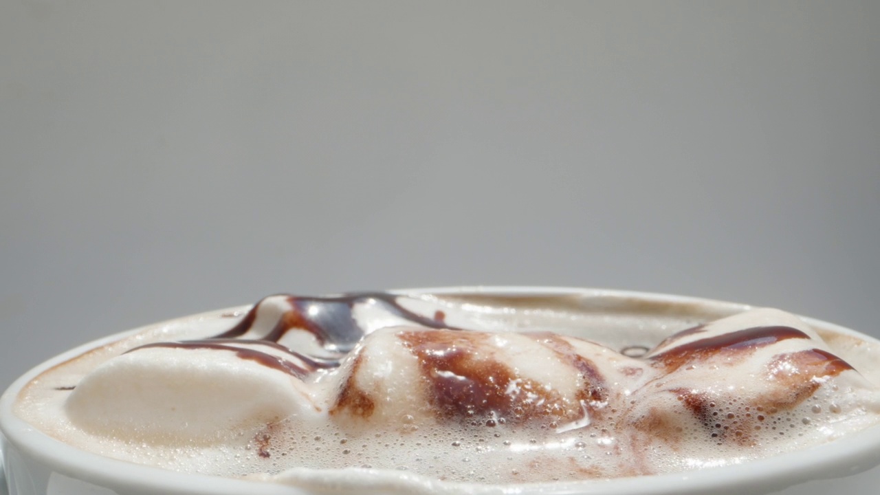 棉花糖淋上巧克力，漂浮在咖啡杯里。我用勺子吃。白色背景。洋娃娃滑块极限特写。视频素材