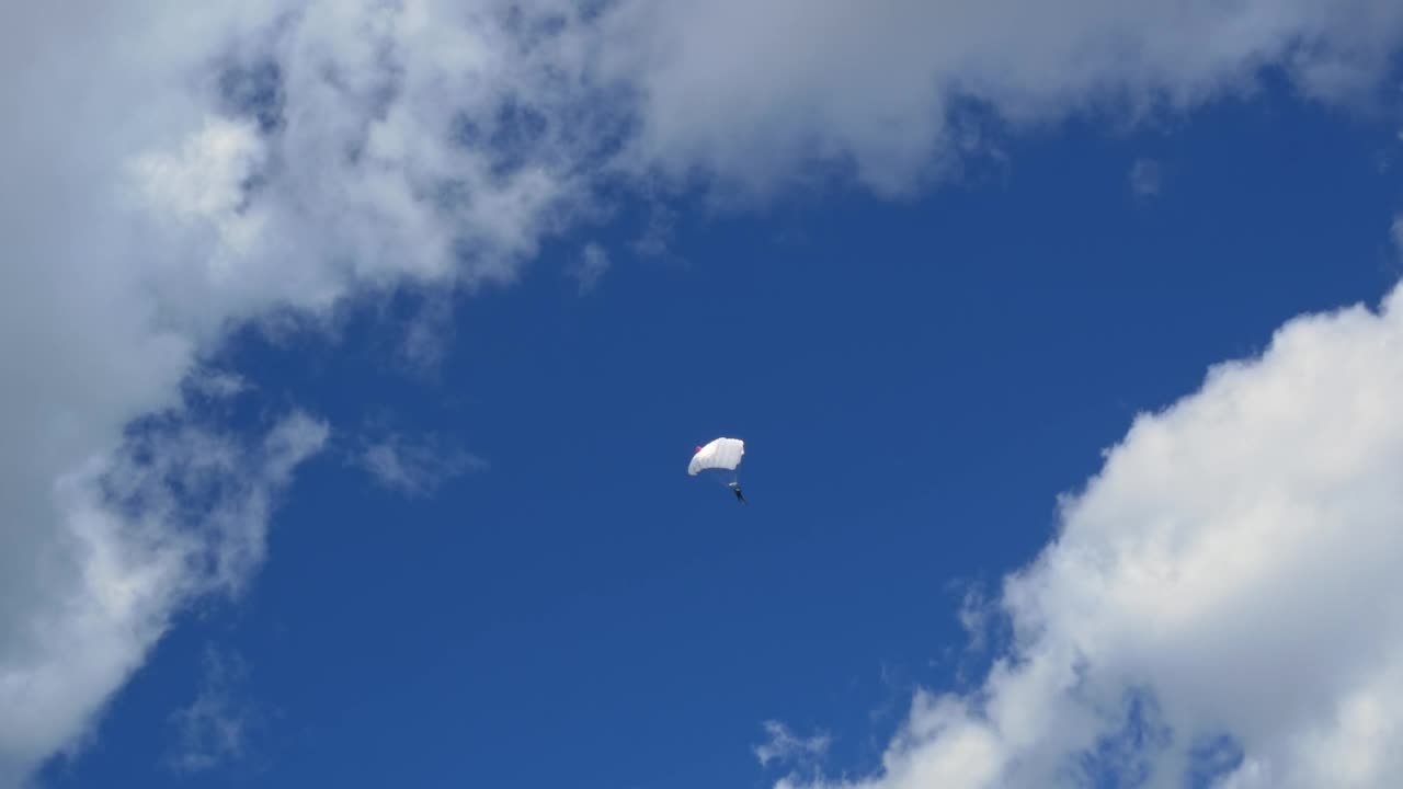 高空跳伞者骑着白色降落伞在美丽的白云间滑翔。无所畏惧的伞兵乘着翼型降落伞像鸟儿一样在高空飞行，以寻找肾上腺素。视频下载