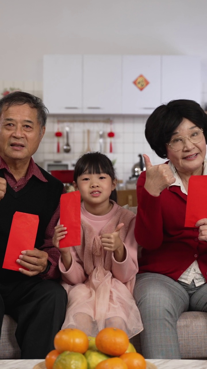 竖屏:中国农历新年，一家混血儿在家里用拇指和胜利的手势对着镜头微笑，用红包压岁钱拍爆棚照。翻译:幸运视频下载