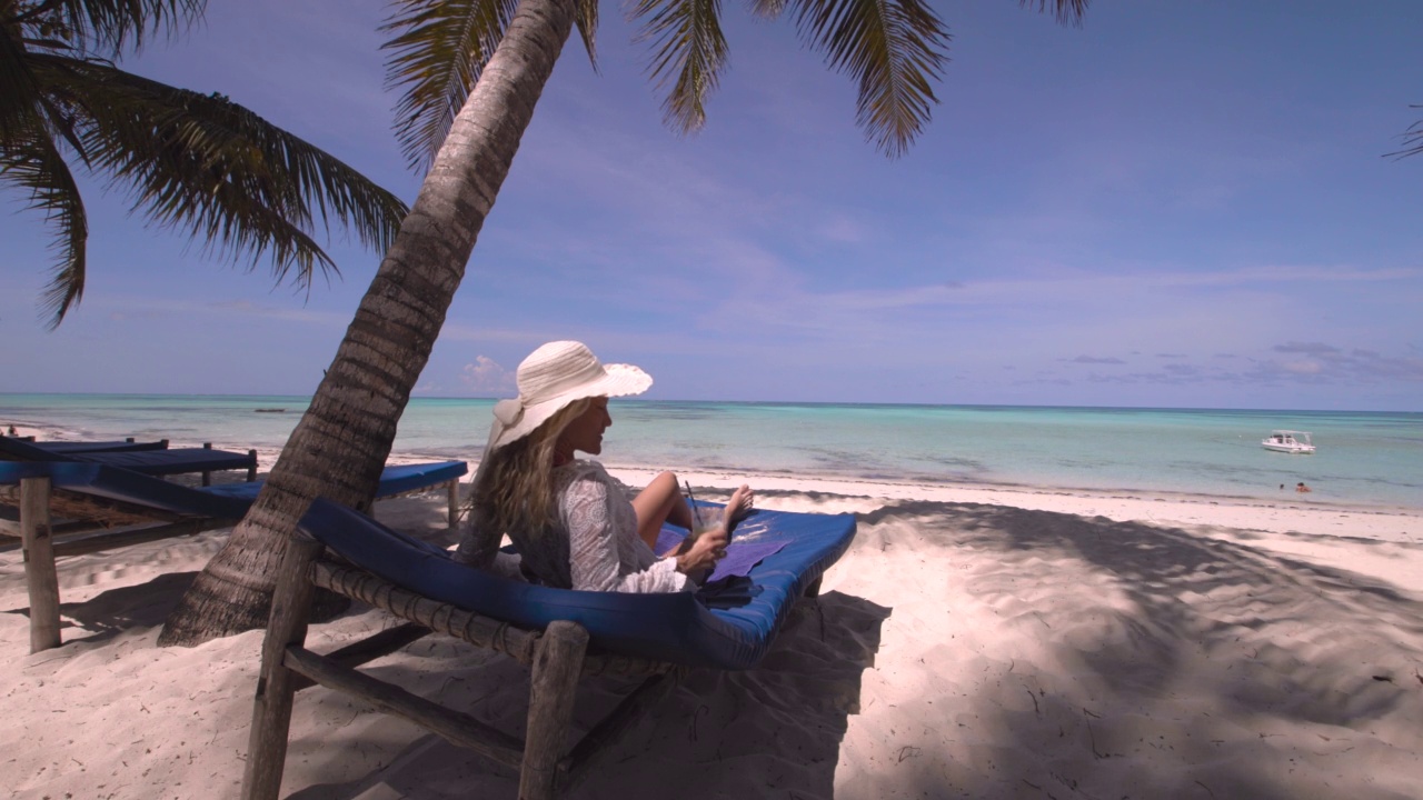 快乐的女人坐在沙滩躺椅上喝果汁。视频素材
