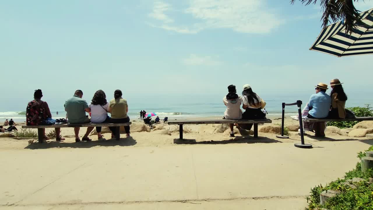 人们坐在海滩上的长凳上视频下载