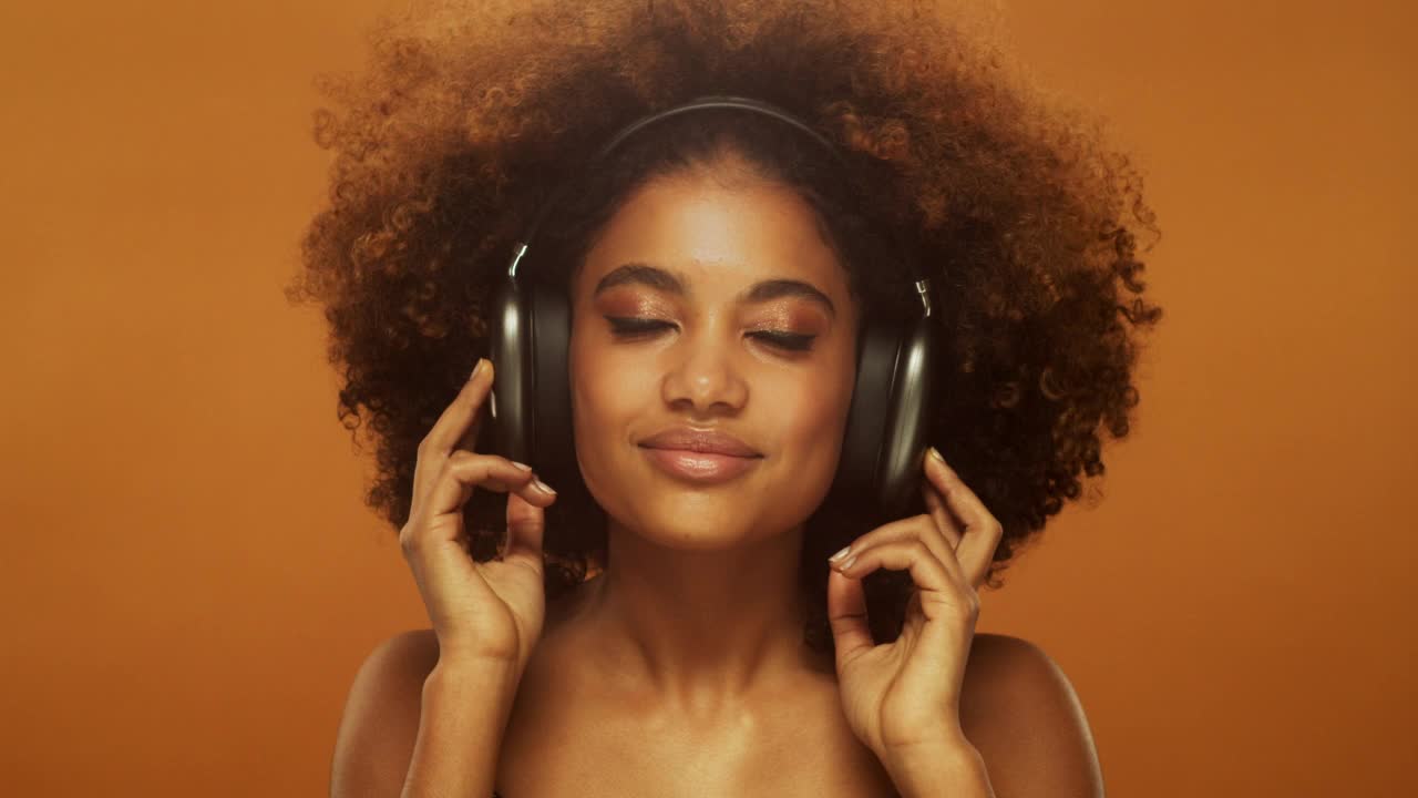 非洲妇女戴着耳机听音乐，被隔绝在棕色的录音棚背景中视频素材