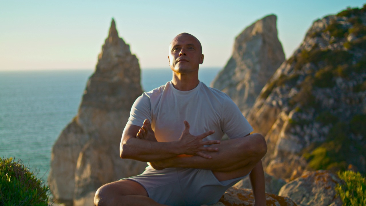 强壮的家伙在美丽的海洋悬崖练习瑜伽特写。专注健康的男人视频下载