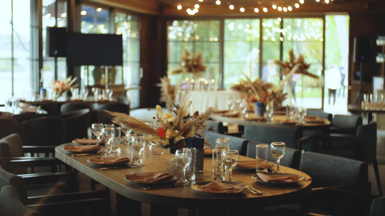 装饰婚礼的餐桌装饰有鲜花、红玫瑰和潘帕斯草，玻璃杯和盘子，相机移动的慢动作。视频素材