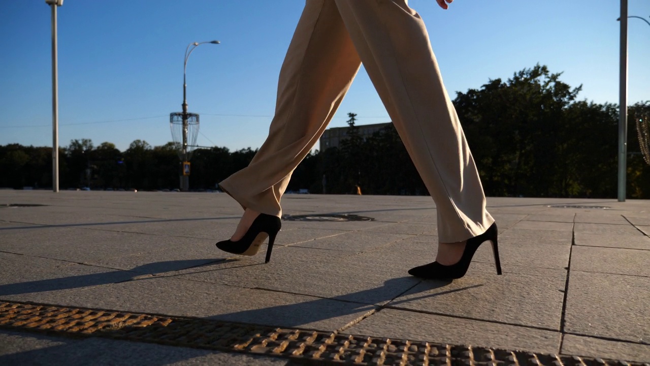 自信的女商人通勤上班。美丽的女士在太阳镜走在人行道上的高跟鞋。迷人的黑发女孩沿着城市街道与太阳耀斑的背景。慢动作视频下载