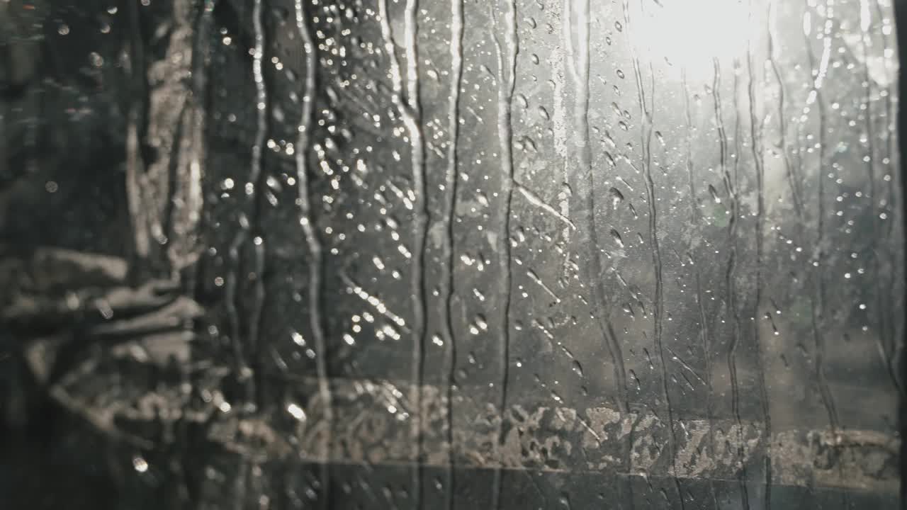 从玻璃上滴下的雨滴特写。小雨滴顺着玻璃流下，映衬着阳光明媚的早晨。水滴从玻璃上流下来。视频素材