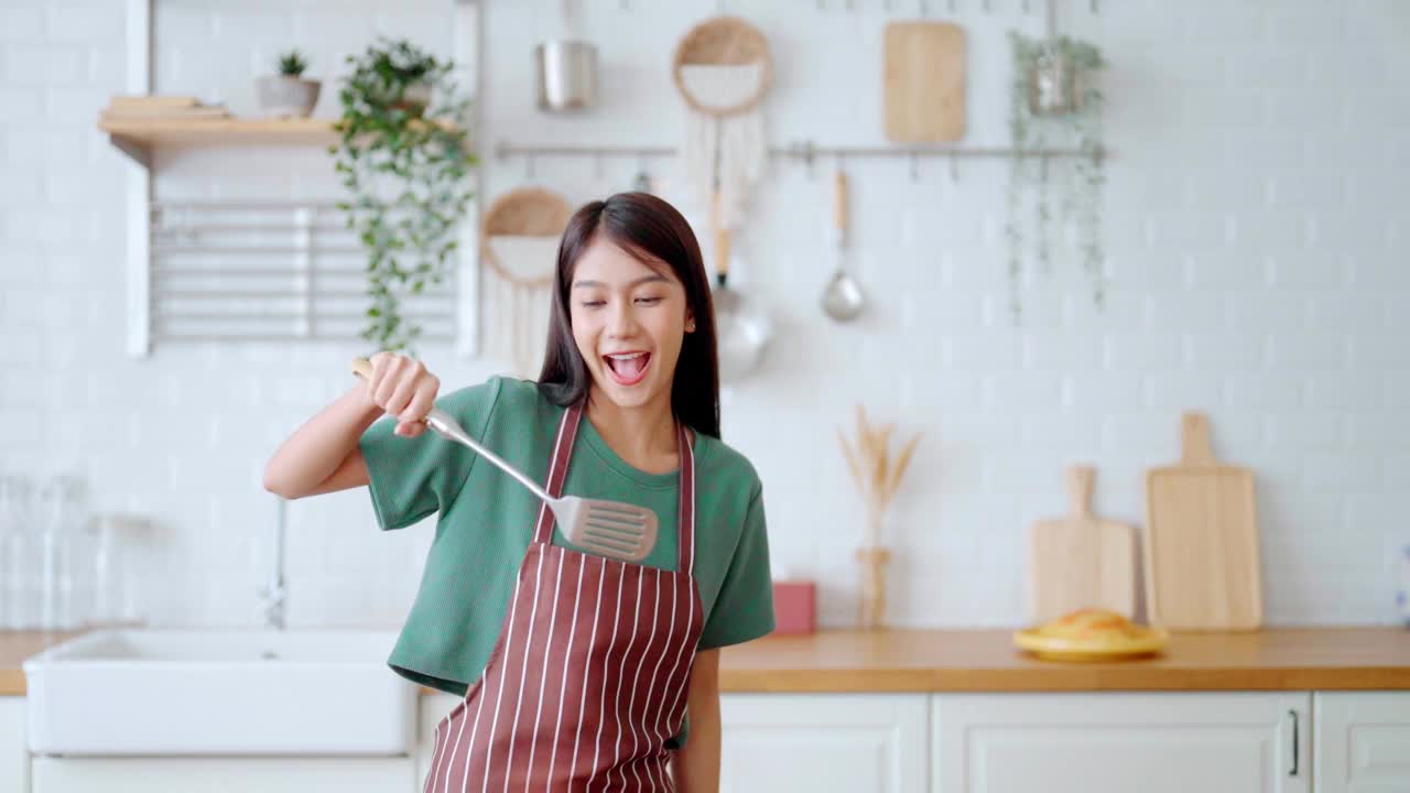 亚洲年轻女子在厨房里跳舞。女性在周末的空闲时间快乐和放松视频下载