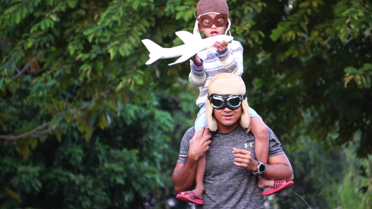 戴着飞行员眼镜的男孩和爸爸在公园里玩飞行游戏视频素材