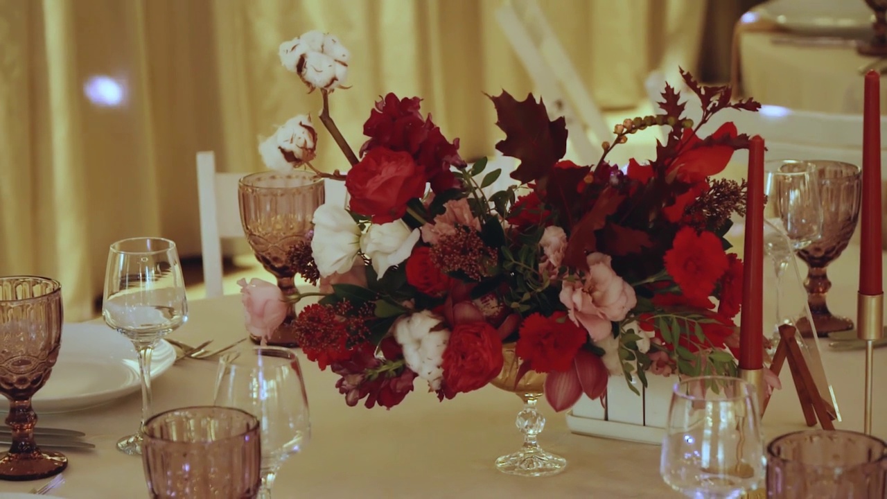 装饰婚礼的餐桌上装饰着一束束鲜花、红玫瑰、喜庆的盘子和玻璃杯，摄像机慢镜头移动。视频素材