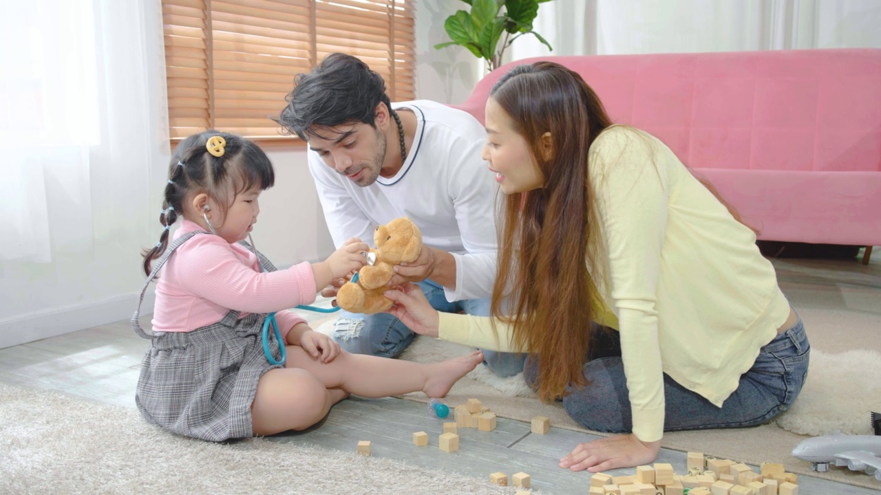 亚洲小女孩玩泰迪熊玩具听他和爸爸妈妈用听诊器，听泰迪熊病人的心跳，享受游戏视频素材