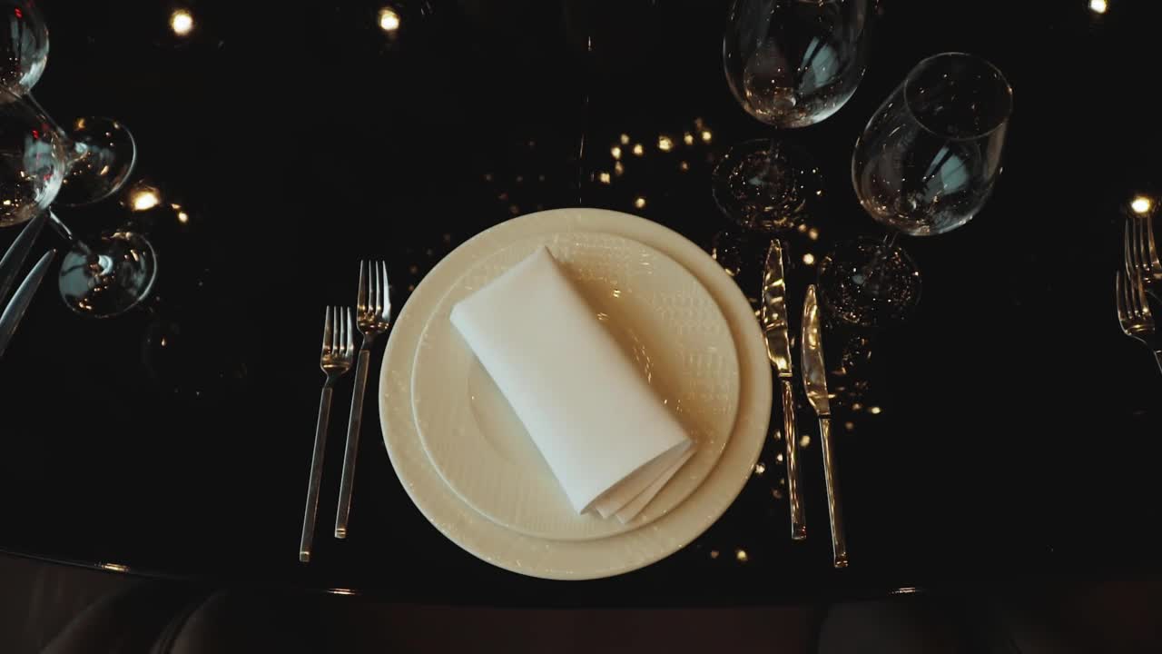 玻璃杯子和白色盘子。餐厅内部的特写餐桌设置。节日餐桌的装饰。盘子放在一张黑色的玻璃桌上。奢华的婚礼，派对，生日。视频下载