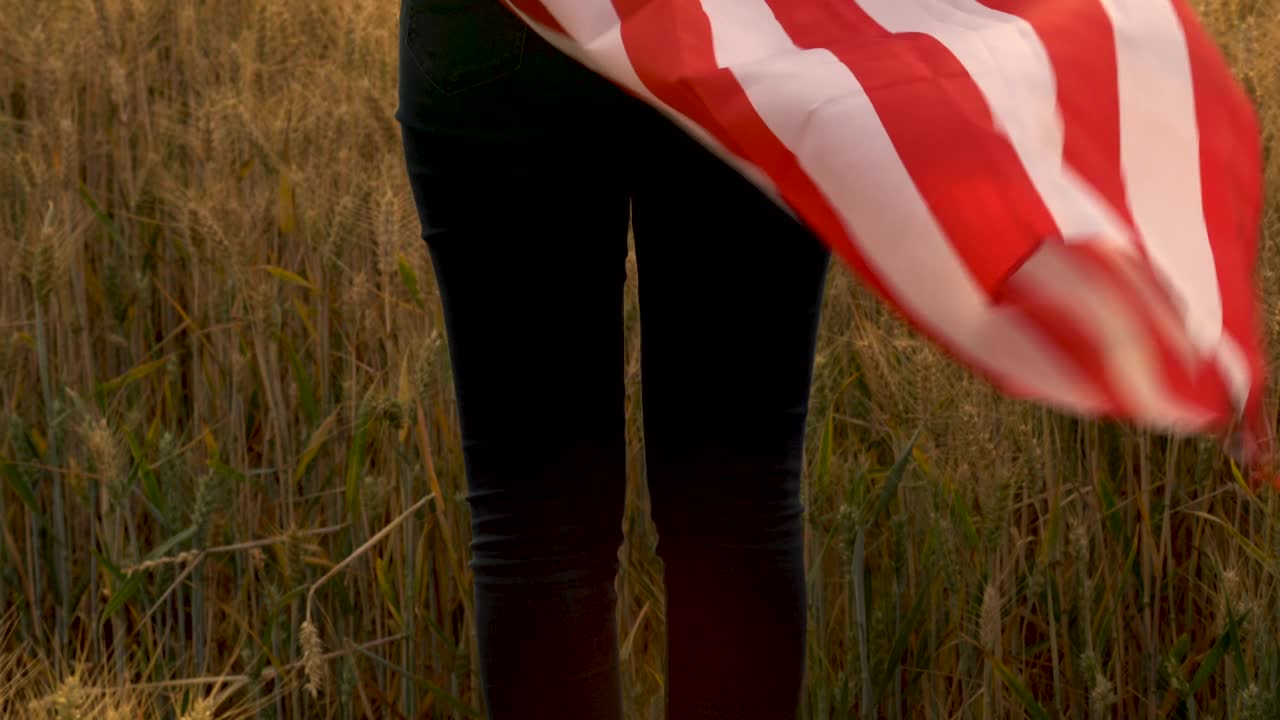 非裔美国女孩，十几岁，年轻的女性，裹着美国星条旗，在日落或日出的麦田里把它举过头顶视频素材