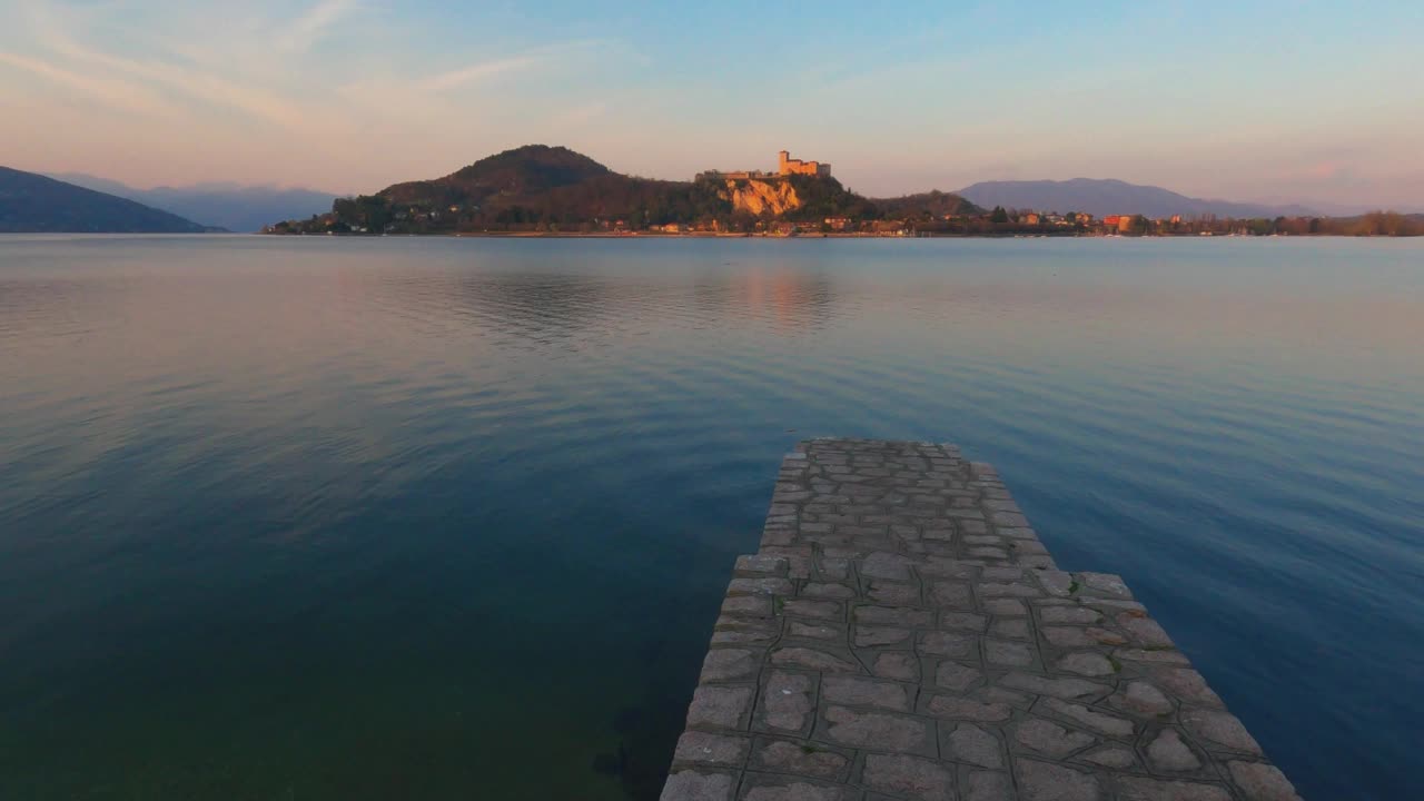 意大利马乔雷湖上平静的水面上的混凝土码头，背景是安杰拉城堡。放大视频素材