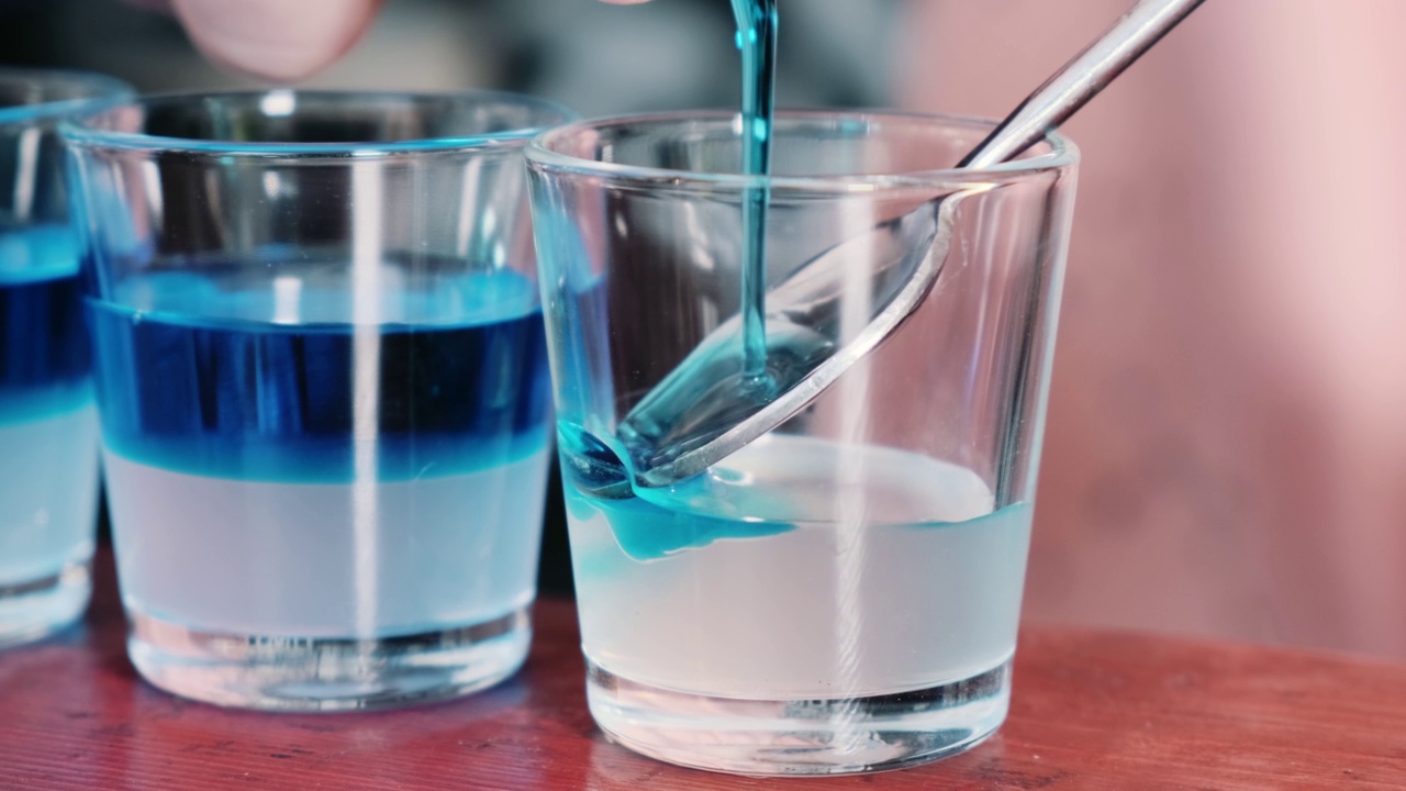 一个酒保往酒里倒蓝色糖浆的特写。一套酒精饮料视频素材