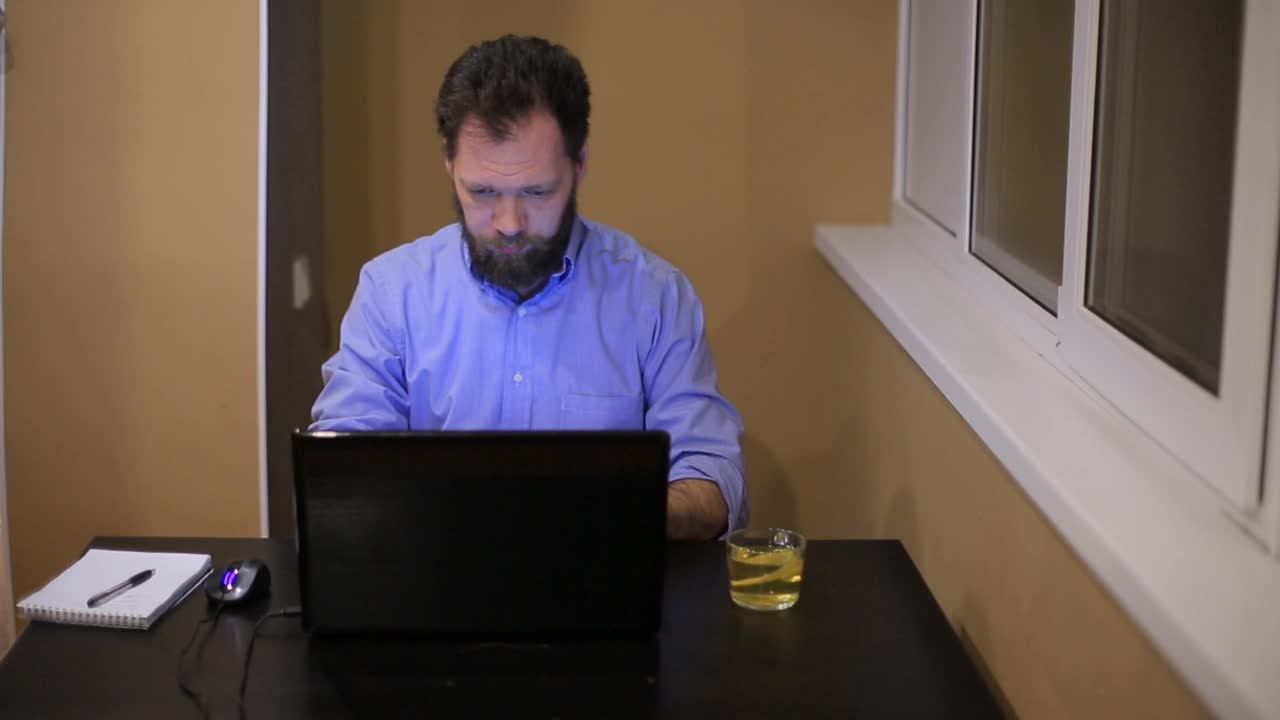 疲惫的商人穿着衬衫，留着胡子，深夜在办公室跑着笔记本电脑视频下载