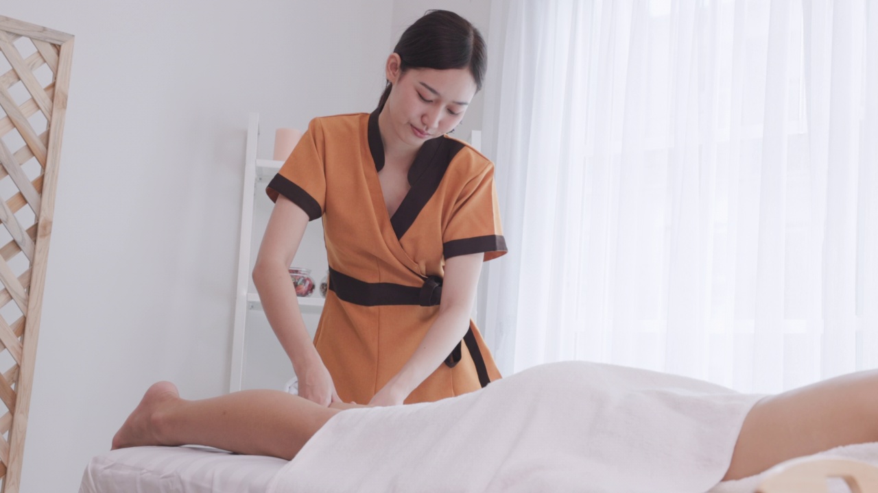 美丽年轻的亚洲女子放松在白色的床上与年轻的按摩水疗治疗专业。泰式水疗沙龙腿部按摩，生活美女人概念。视频下载