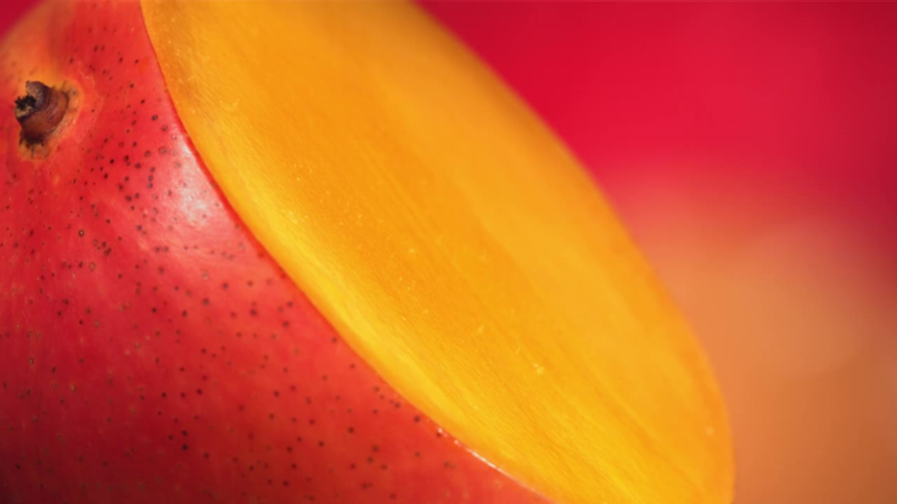 一滴芒果汁顺着旋转的半切芒果王的表面流下。慢动作视频下载