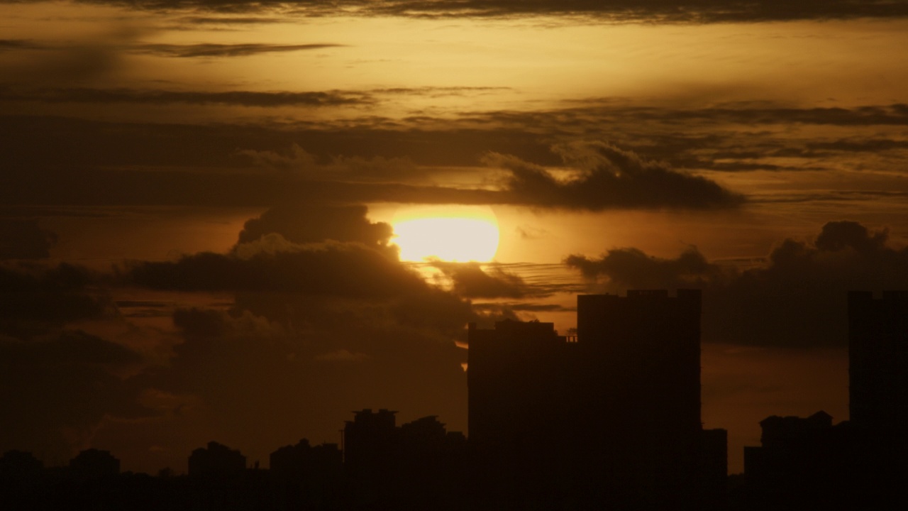 在柔和的夕阳下，天空中的云朵在建筑物轮廓上的时间流逝视频下载