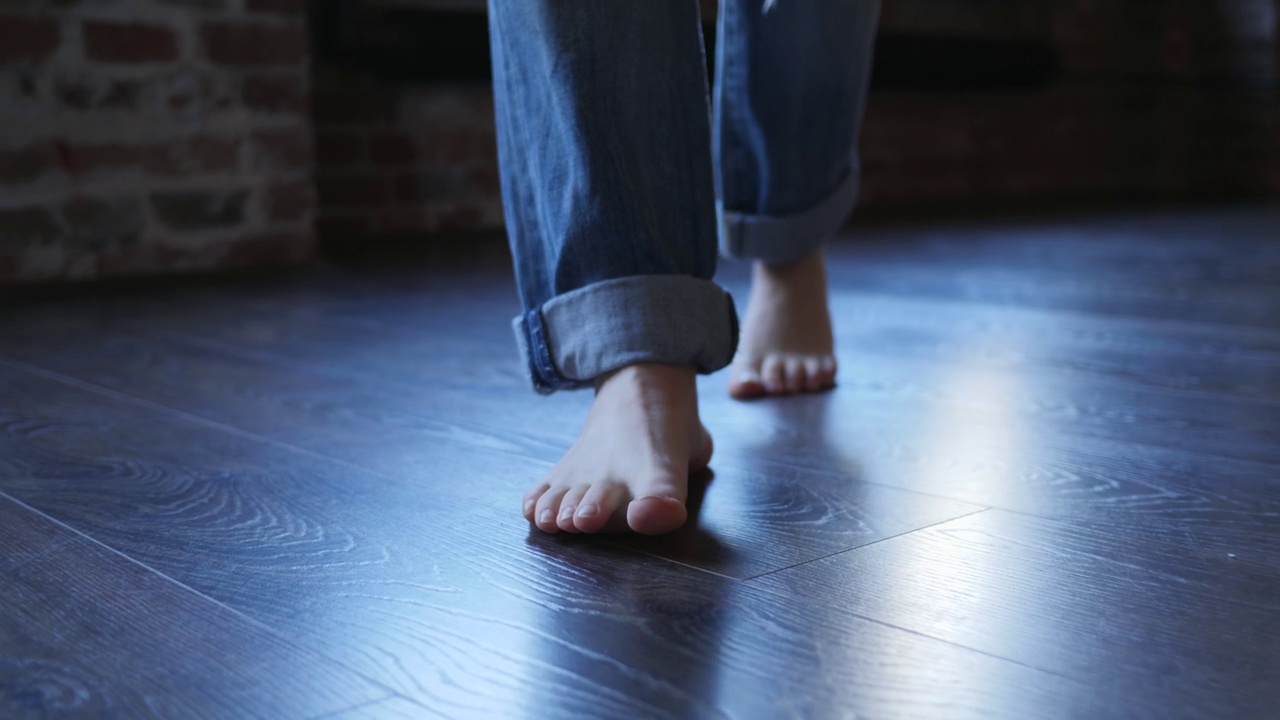 赤脚女孩的腿在牛仔裤裤子走在拼花地板在家里视频下载
