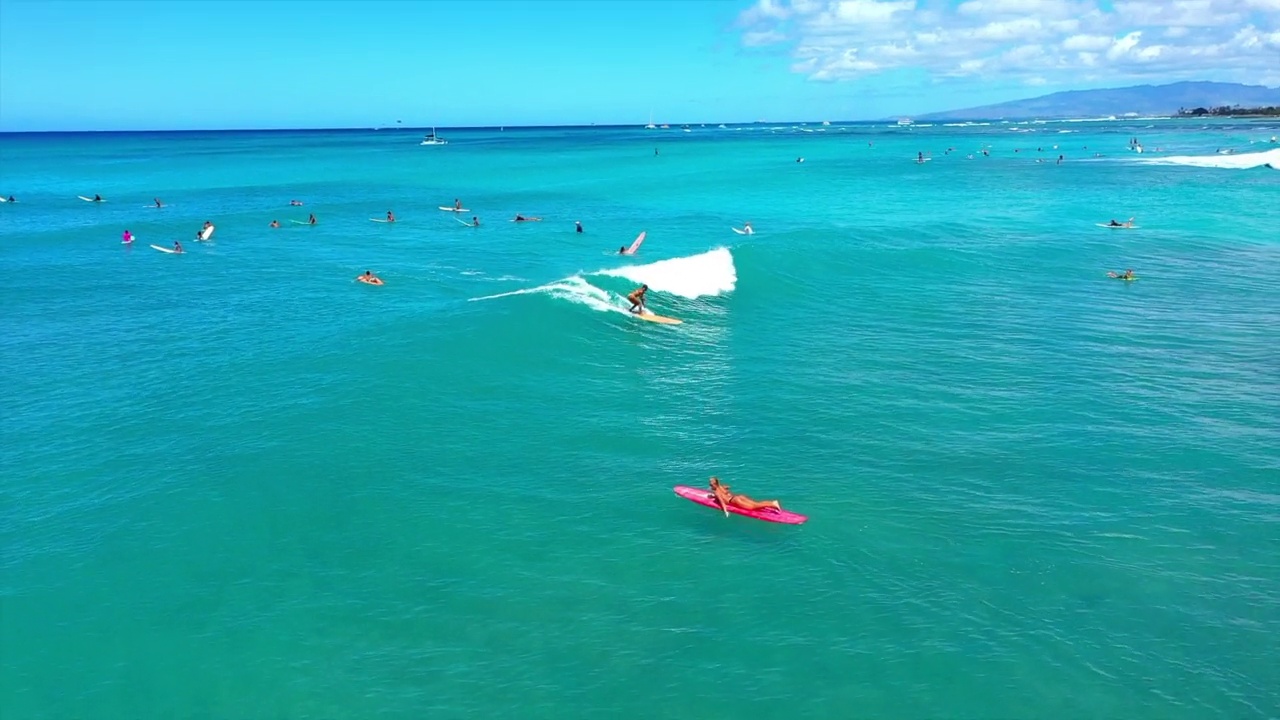 空中拍摄的女人和男人在多云的天空下冲浪在蓝色的大海-怀基基，夏威夷视频下载