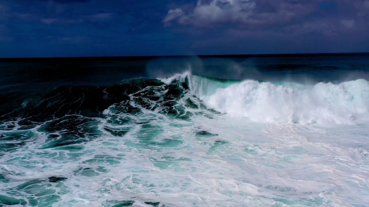 空中拍摄的游客在高浪上冲浪，无人机在云层下向后飞过海面-怀基基，夏威夷视频下载