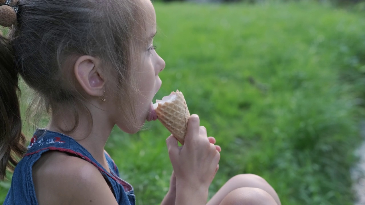 年轻可爱的白人女孩吃冰淇淋，孩子享受冰淇淋，拿着一个冰淇淋蛋卷，吃了一口甜点视频下载