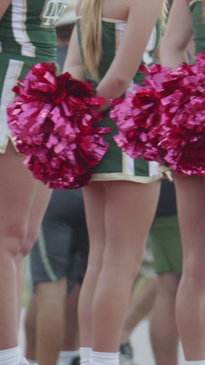 啦啦队队员在美式橄榄球比赛中拿着粉红红色的球球欢呼。-垂直格式视频下载