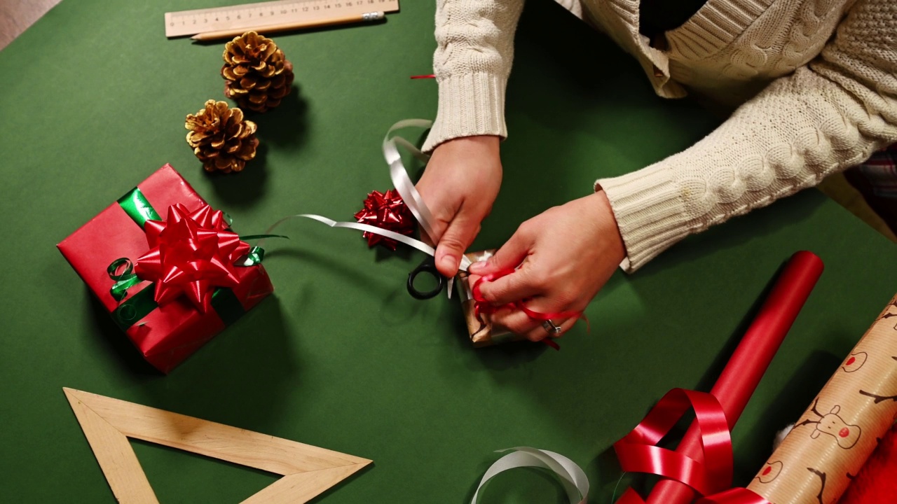 俯视图的一个女人的手用剪刀，切割白色装饰丝带在条状，而绑一个圣诞礼物视频素材