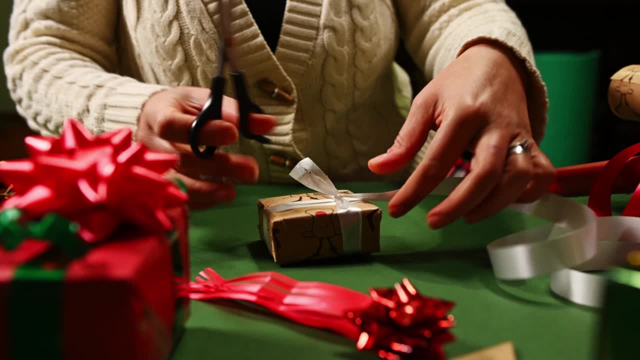 自制的礼物。圣诞节和新年的准备。特写女人包装圣诞礼物，用白色和红色丝带系一个蝴蝶结视频素材