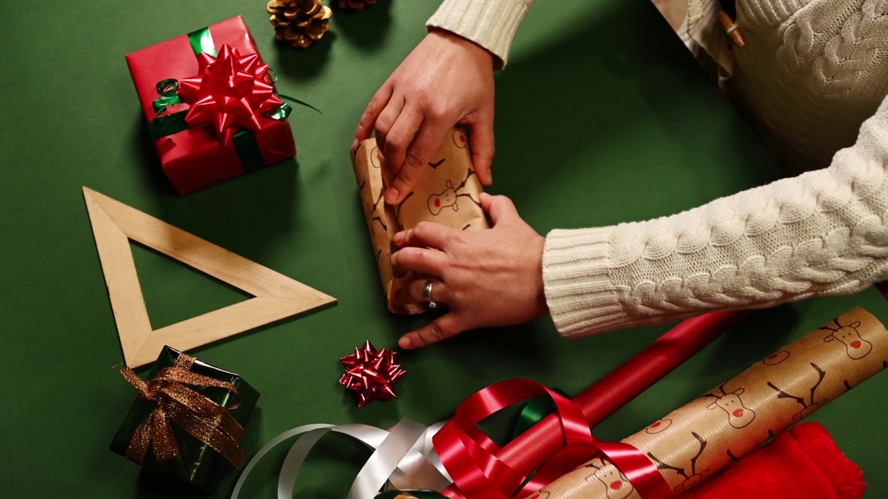 特写的妇女的手包装礼物在一个绿色表面上有鹿图案的包装纸。圣诞快乐视频素材