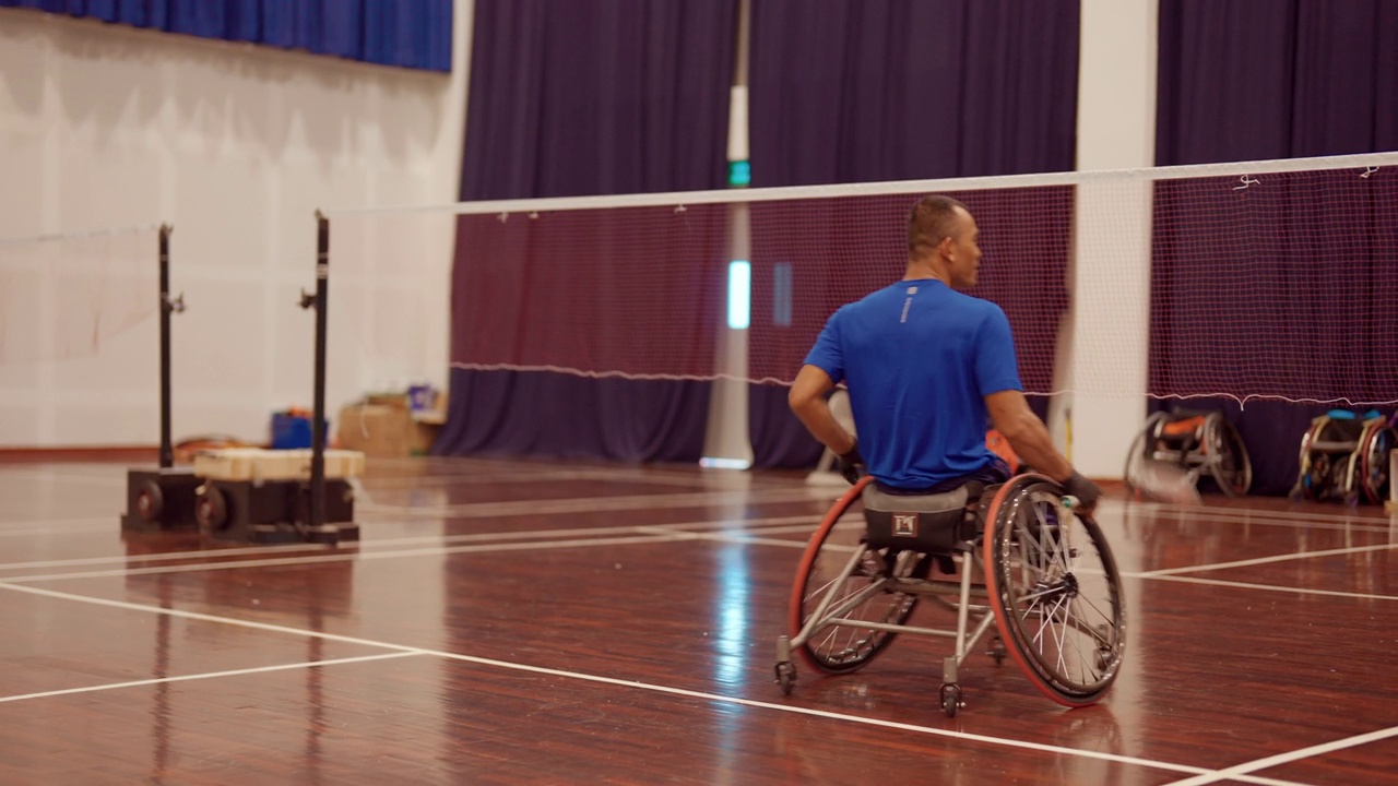 亚洲男子在室内网球场打和练习轮椅羽毛球。视频下载
