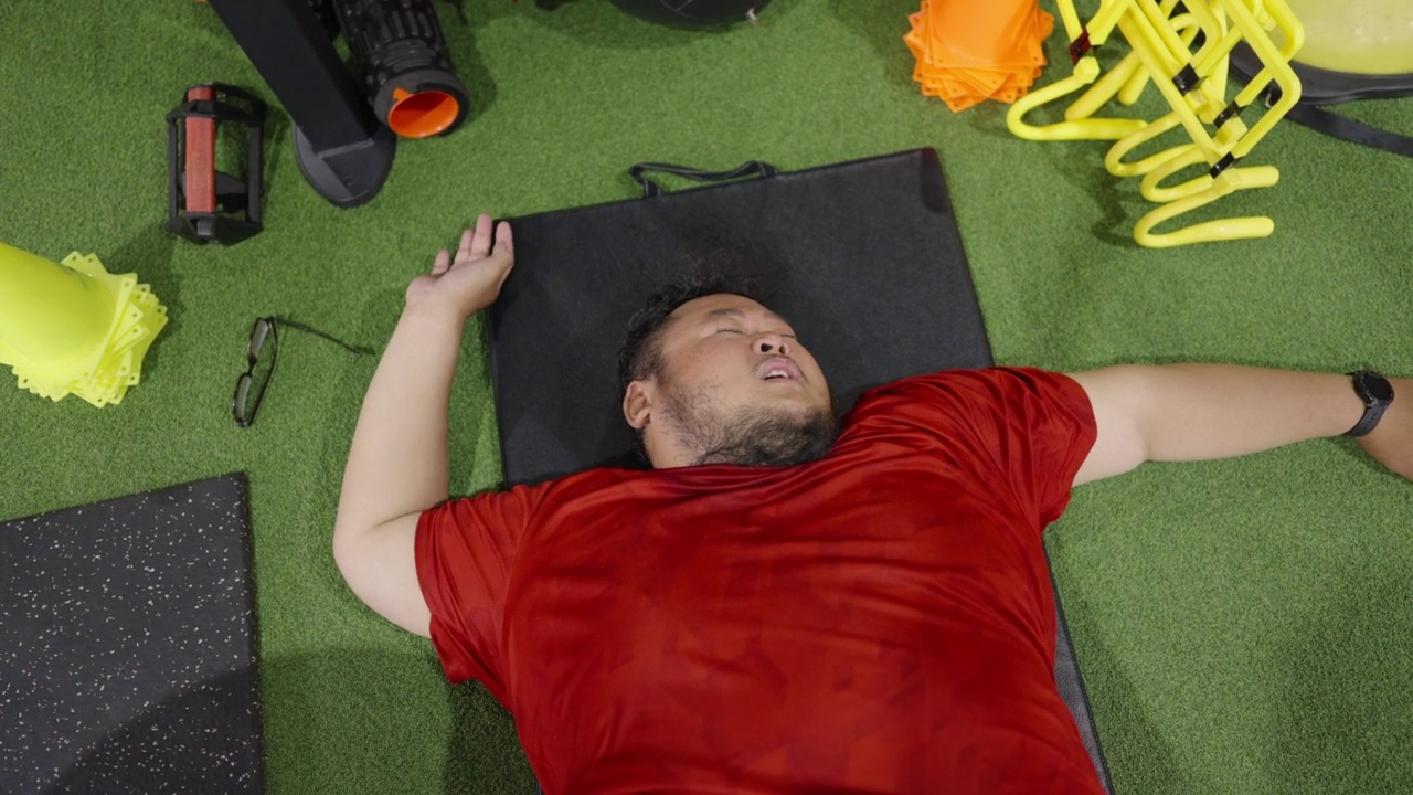 俯视图视频的一个大男子喘气，躺在一个健身房的运动垫上。视频素材