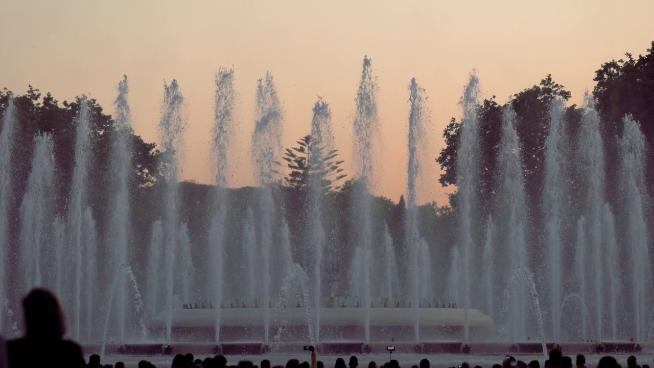 日落前拍摄的在西班牙加泰罗尼亚的巴塞罗那蒙特juic歌唱魔术喷泉的表演。在前景剪影的人。高质量4k镜头视频素材