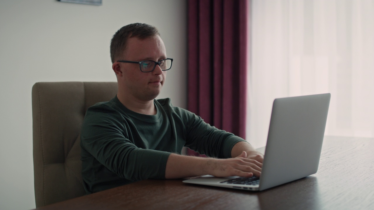患有唐氏综合症的成年白人男子在家里使用笔记本电脑。用红色氦相机在8K拍摄。视频下载