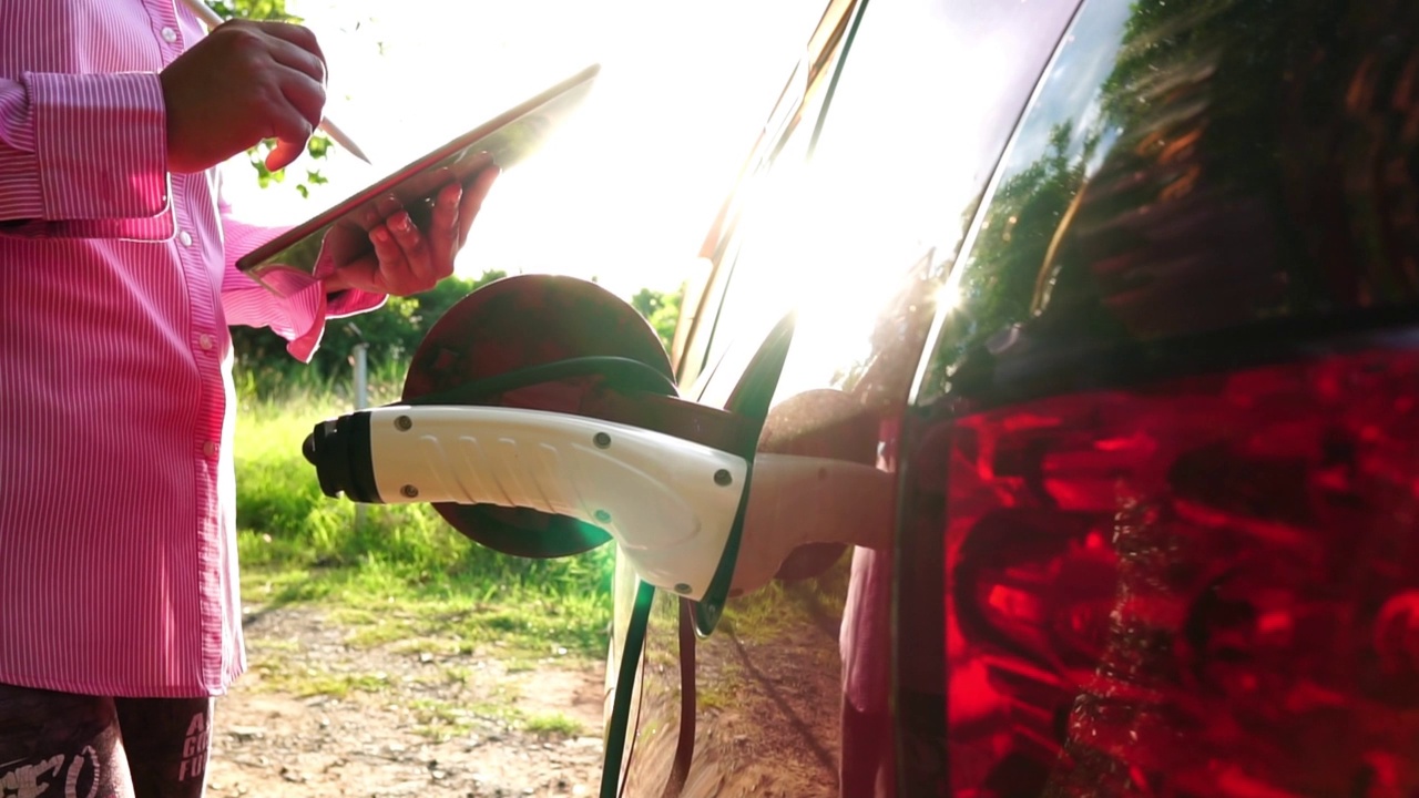 一位女士在绿色能源充电站等待她的汽车充电时使用智能手机视频素材