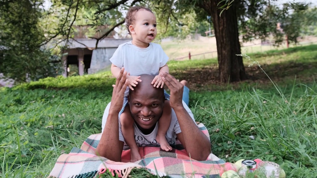 一个快乐的非裔美国爸爸和一个小孩在公园的草地上玩耍视频下载