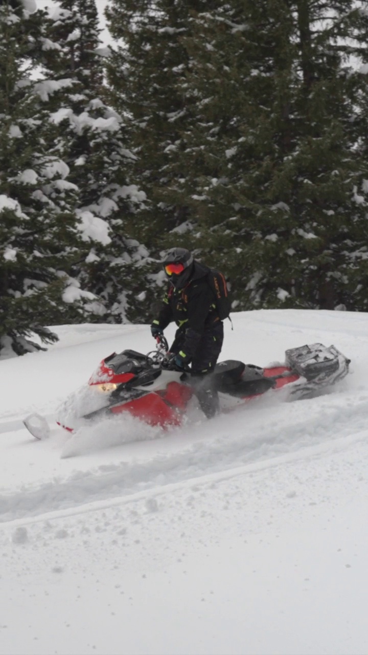 一名驾驶雪地摩托的女子骑着一辆红色的雪地摩托撞在了山上的雪地上。-垂直格式视频下载