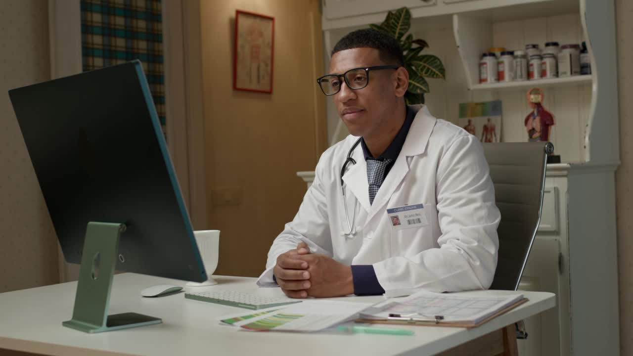 医生在线咨询病人。非裔美国医生坐在医院办公室接受视频通话。视频素材