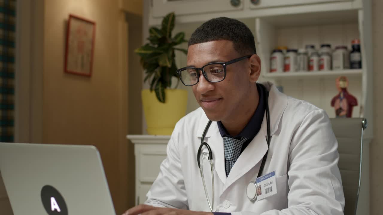 医生与病人进行视频通话。非裔美国执业医师坐在医院办公室里用笔记本电脑上网工作。视频素材