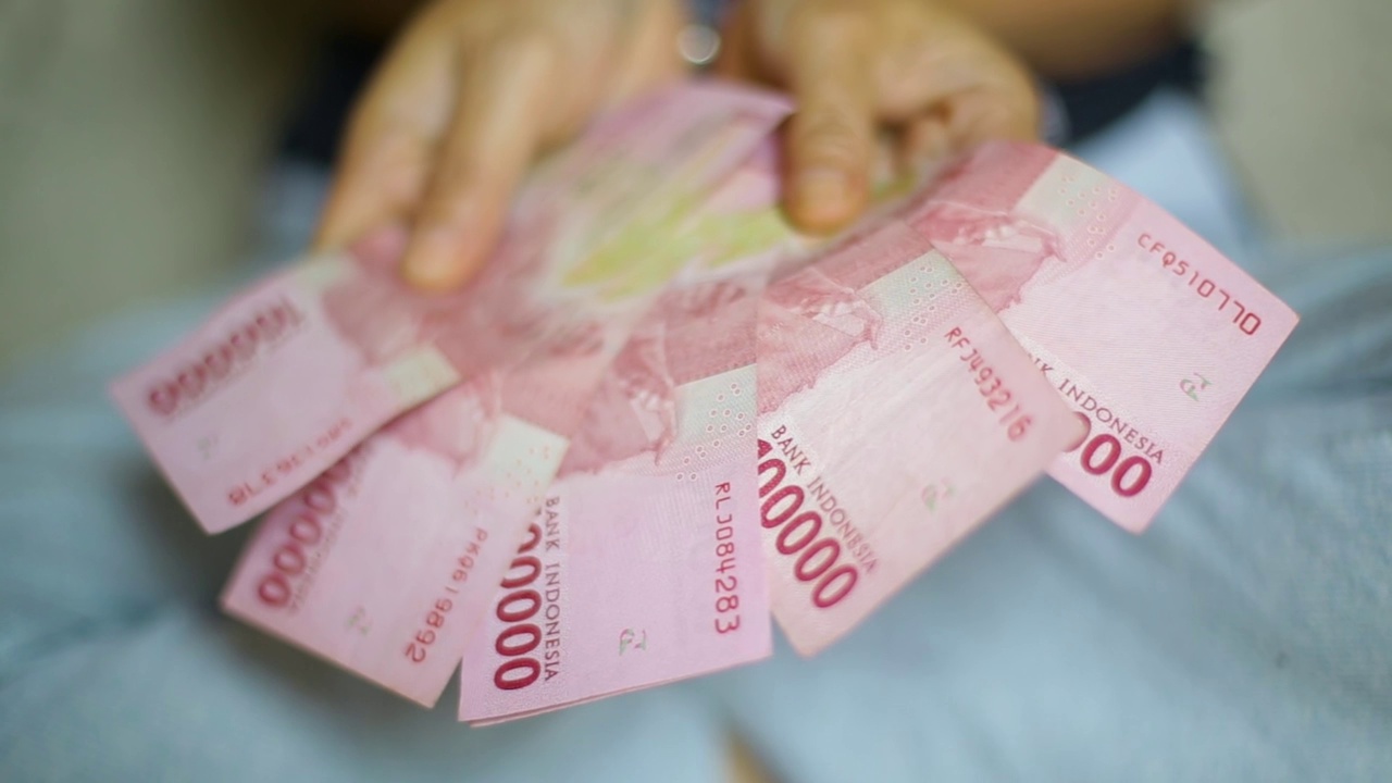 一名亚洲女性手里拿着一串串的印尼卢比(IDR)红10万纸币。印尼纸币视频下载