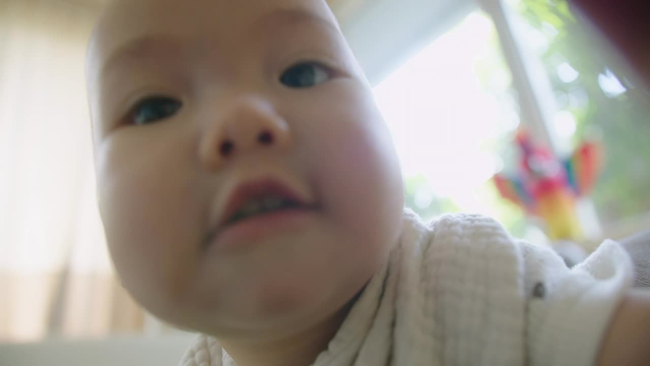 肖像的脸可爱的小女婴看着感兴趣和惊讶的抓拍相机镜头，爸爸拍摄的婴儿在家里的客厅蹒跚学步视频素材