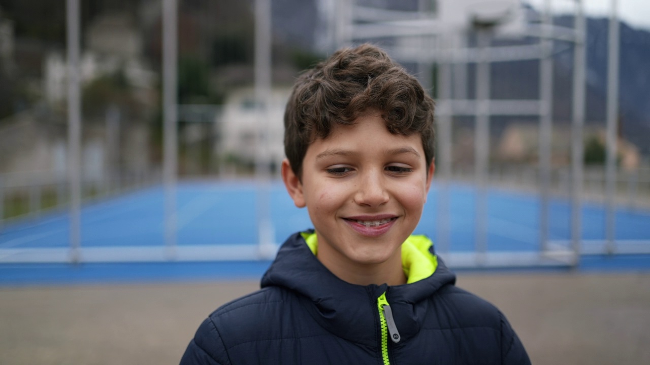 一个快乐的英俊的年轻男孩站在户外的城市公园微笑。肖像脸特写的前十几岁的男孩穿着冬天的衣服视频下载