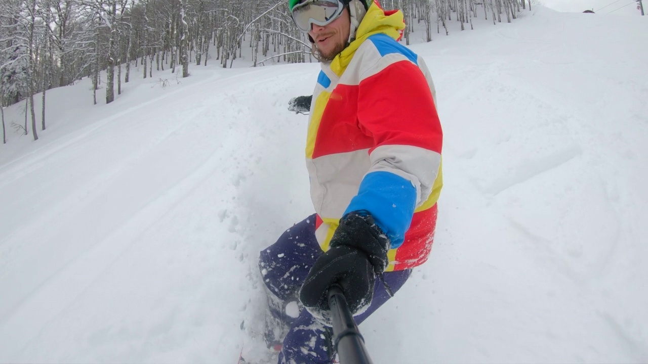 慢动作自拍视频。一个穿着彩色夹克的年轻人在厚厚的积雪上骑着滑雪板视频素材