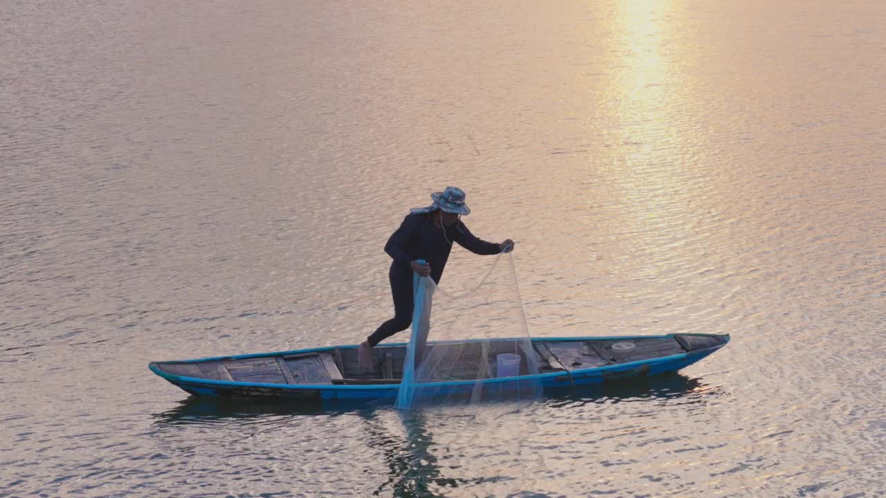 夕阳西下时，湖上的渔船上正在工作的渔民们拉着渔网离开水面视频素材